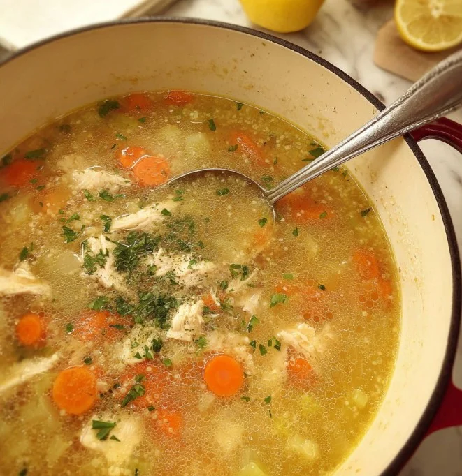 Bowl of lemon chicken quinoa soup garnished with herbs and lemon slices