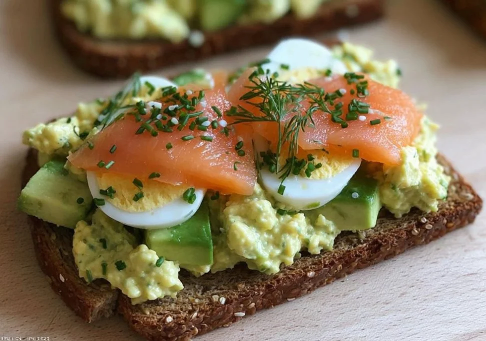 Avocado egg salad and salmon sandwich on a plate garnished with fresh herbs